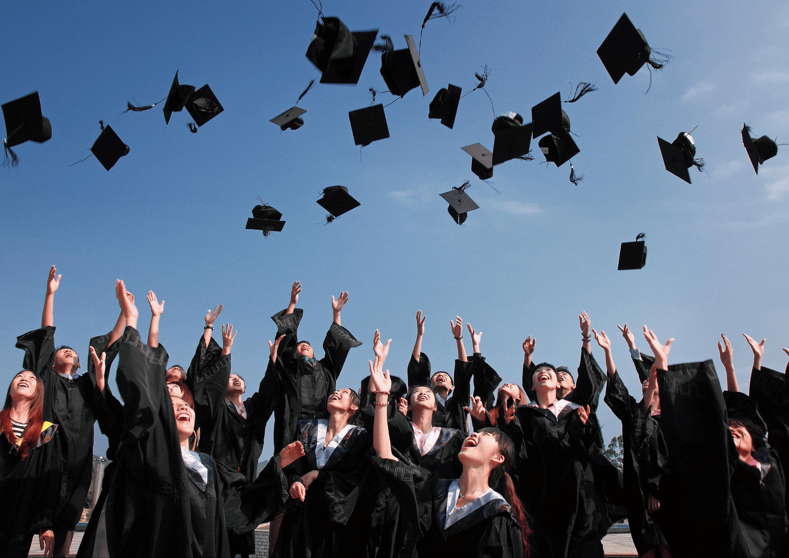 June Graduation Season: A large group of excited graduates throwing their caps into the blue sky during convocation.