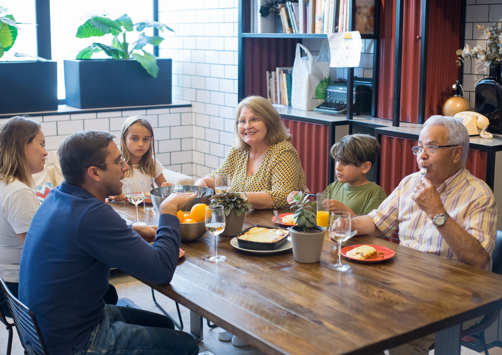 A multi-generational family sharing a home-cooked meal around a dining table, illustrating a family gathering hosted by in-laws.