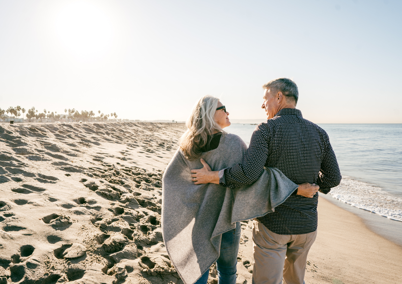 Older couple embracing and looking at each other while walking along the ocean shoreline.