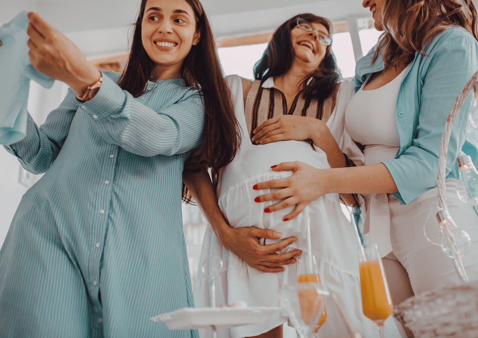 Office Baby Shower Gift Ideas: Coworkers smiling around a pregnant colleague at a party with drinks and baby clothes.