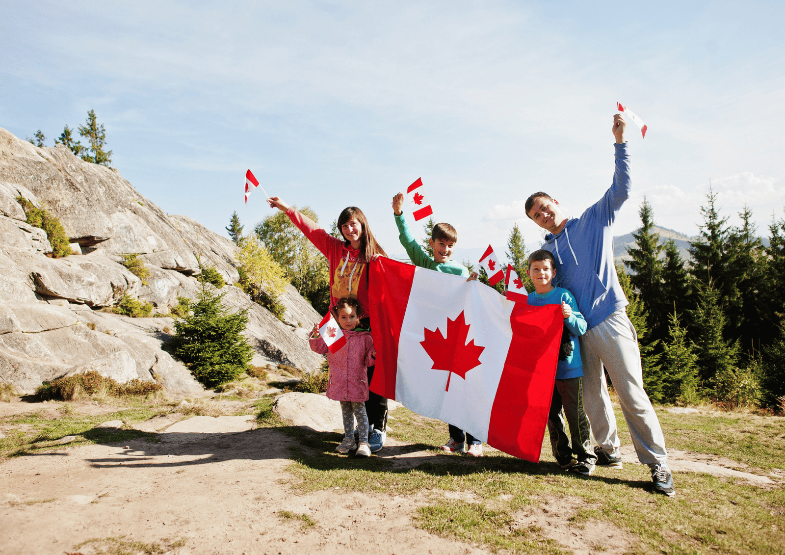 Canada Day Gift Delivery Guide: A happy family holding a large Canadian flag and waving small flags outdoors in a rocky, forested landscape.