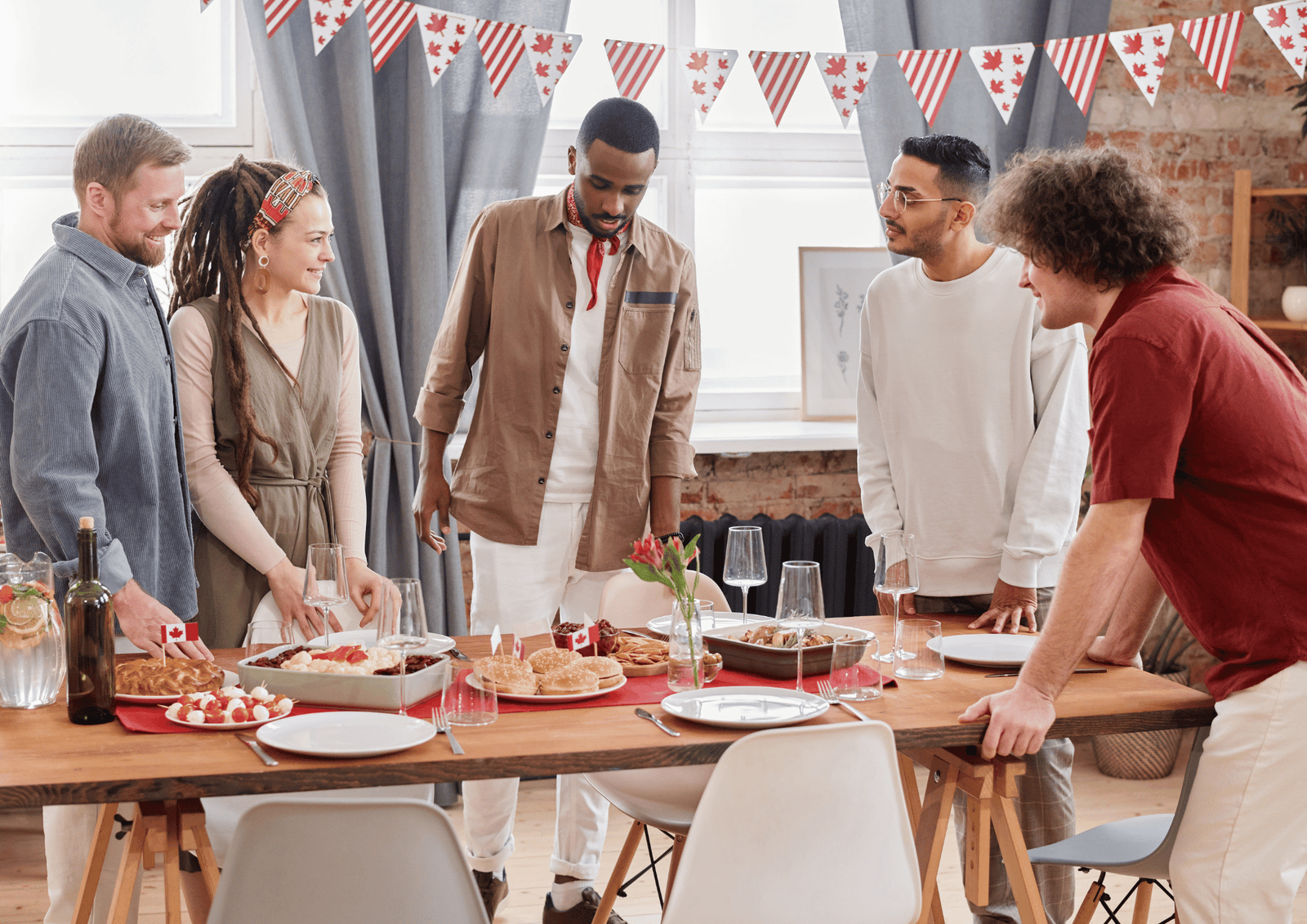 Corporate Canada Day Gifts: A diverse group of colleagues gathering around an office table with food, drinks, and Canadian flags.