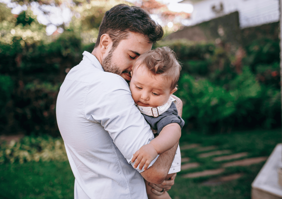 Father's Day Gifts for New Dads: A loving father tenderly hugging his baby boy outside in a backyard garden.