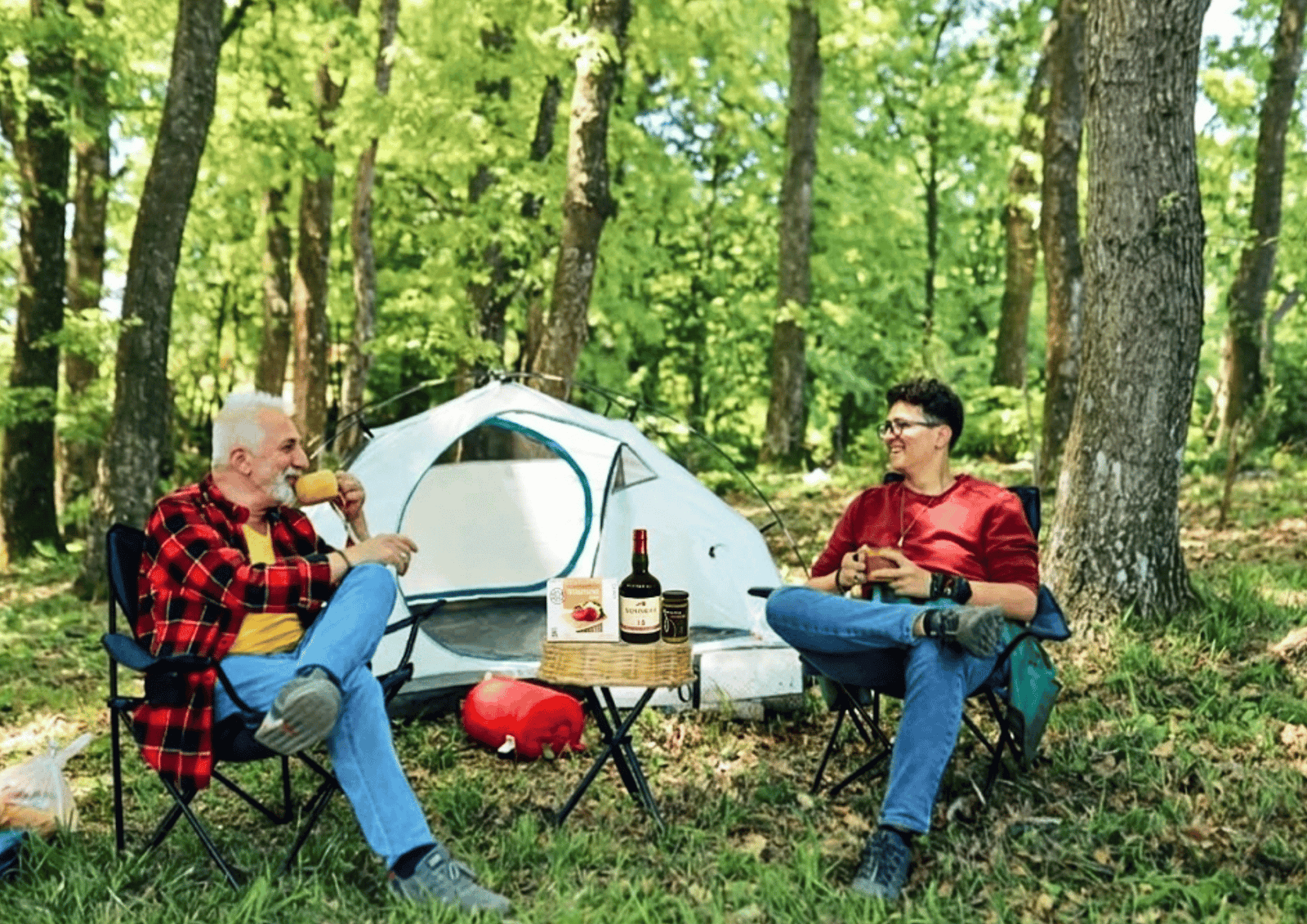 A happy senior father and adult son clink glasses together outdoors, celebrating Father's Day.