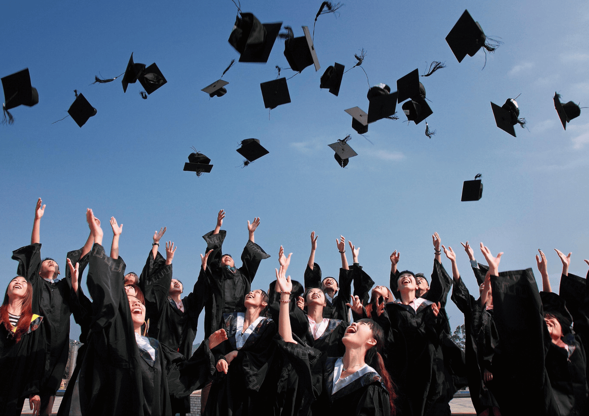 June Graduation Season: A large group of excited graduates throwing their caps into the blue sky during convocation.