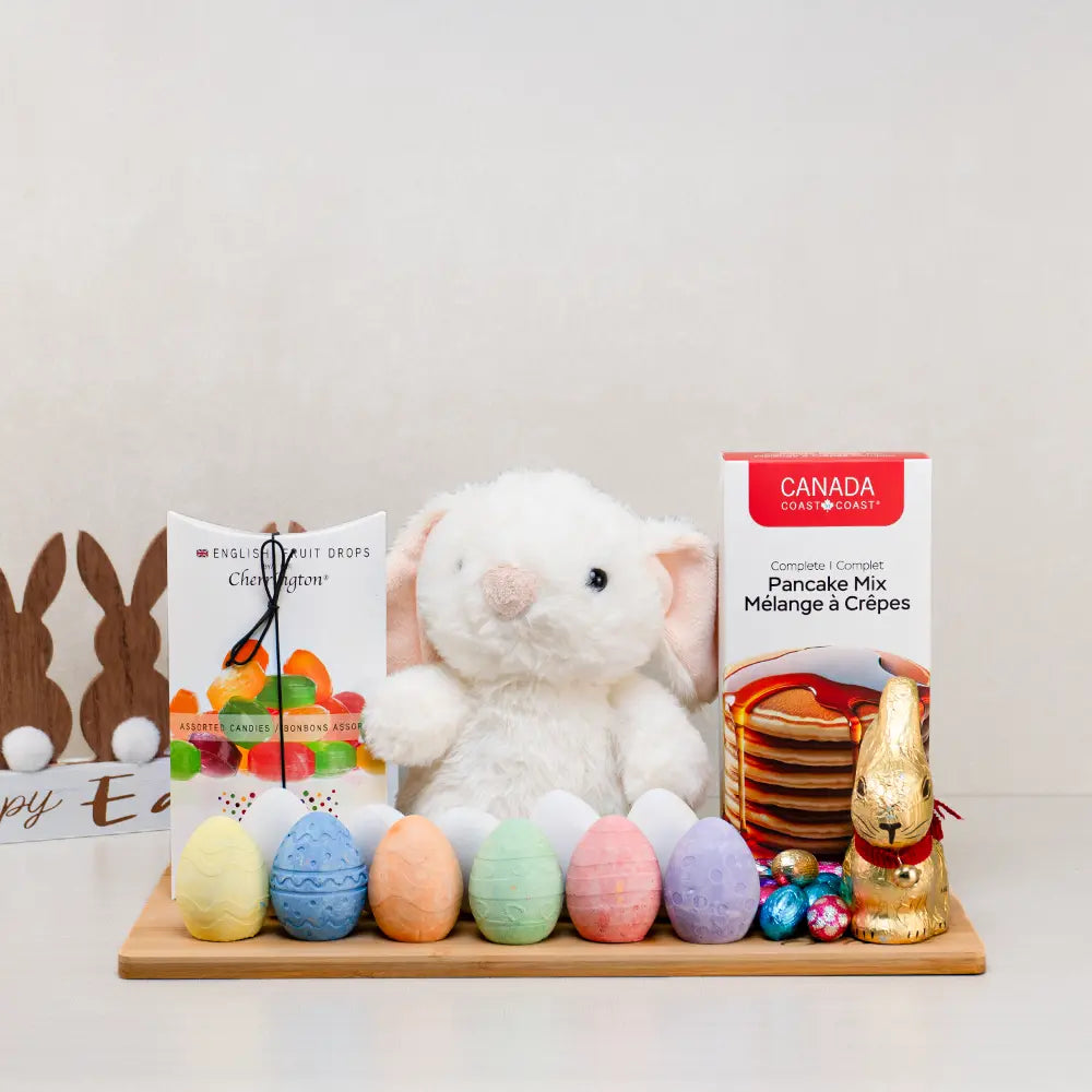 Baby's First Easter Gift Basket with a white plush bunny, pastel chalk eggs, gold foil chocolate bunny and pancake mix