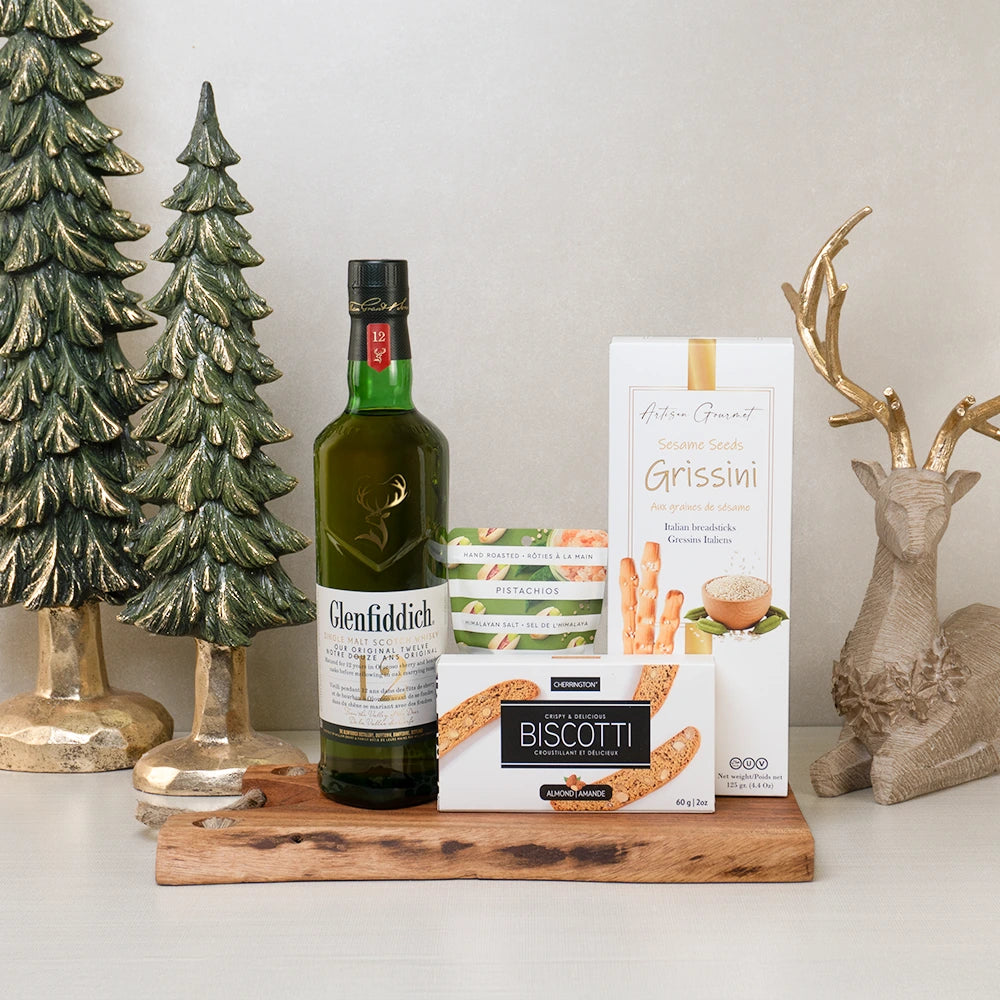 Alcohol gift basket with scotch whiskey, pistachios, biscotti, and breadsticks on a wooden board, perfect for Christmas.