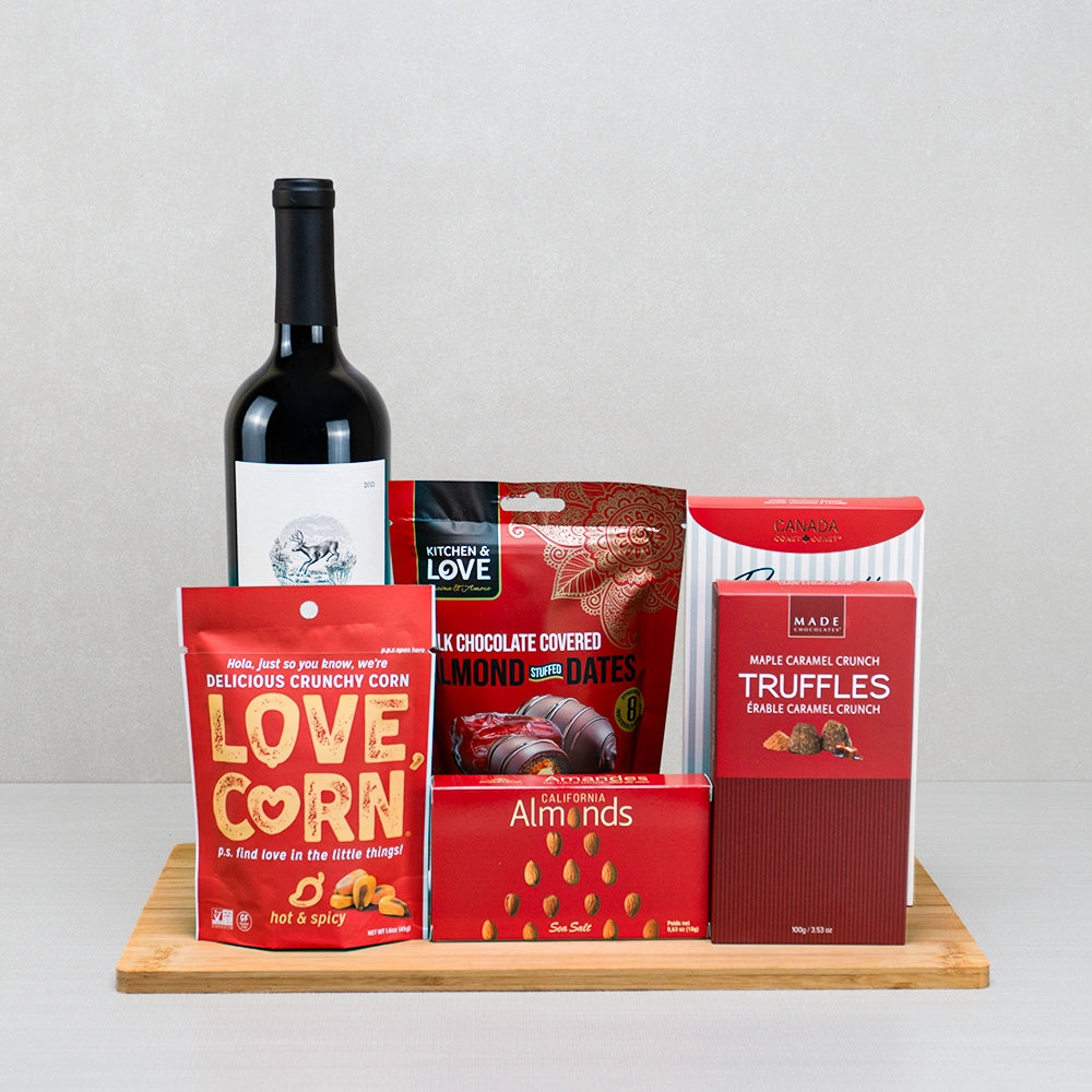 Tastes of Comfort Wine Basket with red wine, Love Corn, chocolate almond stuffed dates and maple caramel truffles on bamboo