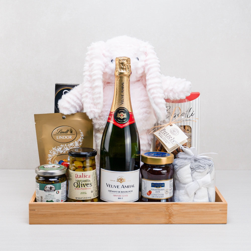 Newborn Celebration Gift Basket with Veuve Ambal Crémant, a pink plush bunny, Lindt Lindor and washcloths on a bamboo tray