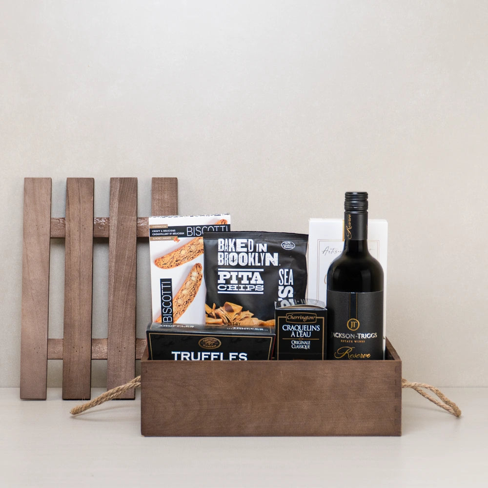 Red wine gift crate with raspberry truffles, almond biscotti, breadsticks, and crackers in a wooden crate.