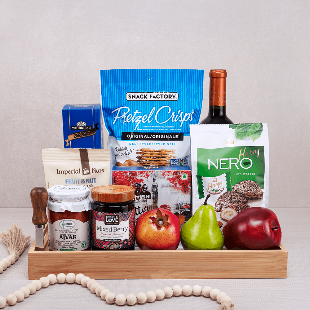 Happy Hanukkah Wine & Snack Basket with red wine, pretzel crisps, nut wafers, ajvar and a fresh pomegranate in a bamboo tray